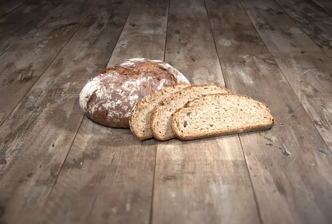 Ein Laib Brot liegt auf einem Holztisch, daneben vier Scheiben. Die ideale Kerntemperatur Brot ist erreicht.