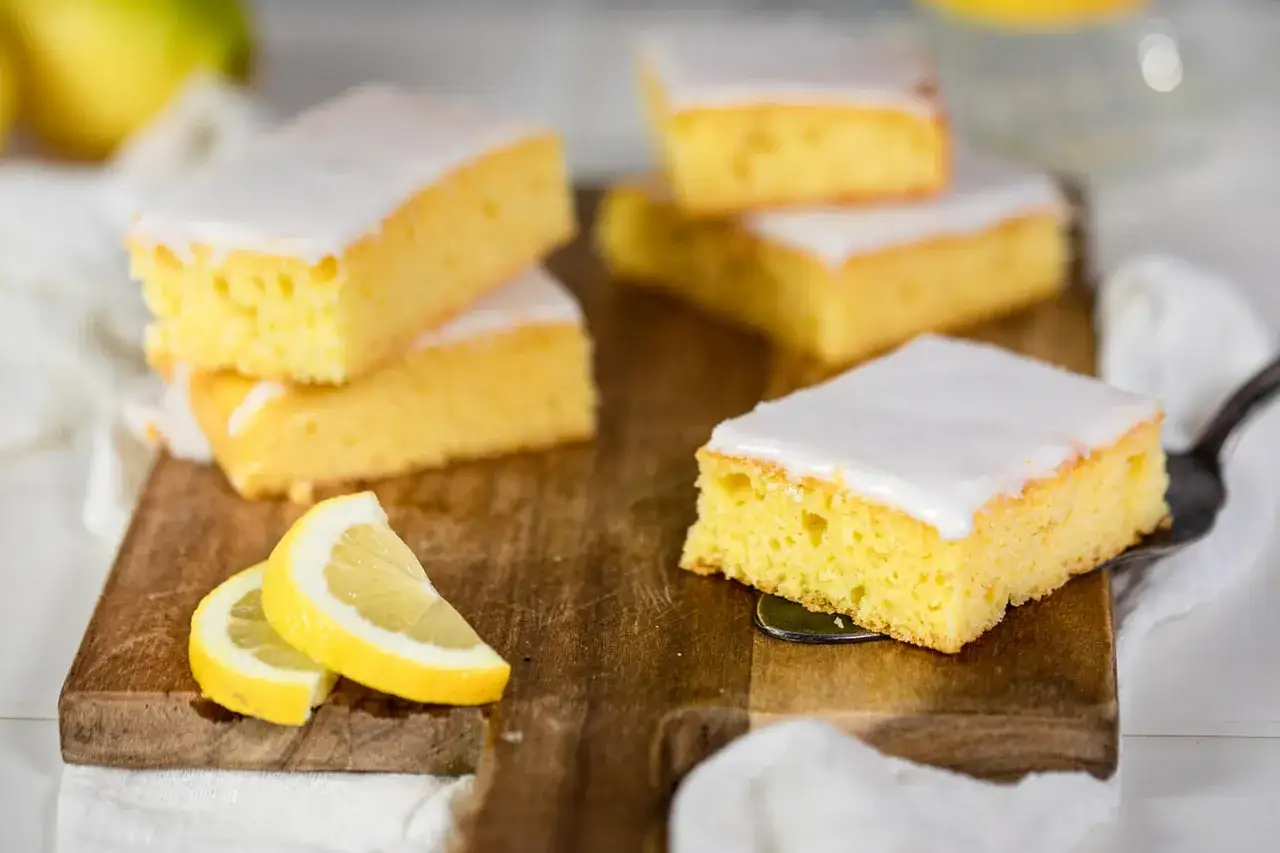 Saftiger Selterwasserkuchen im Tassenrezept-Stil, mit Zuckerguss und Zitronenspalten auf einem Holzbrett.