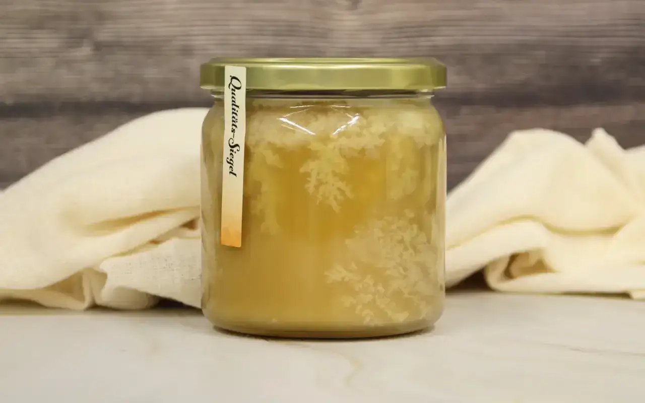 Glas mit honig kristallisiert, zeigt natürliche Kristalle. Das Qualitätssiegel ist auf dem Etikett zu sehen.