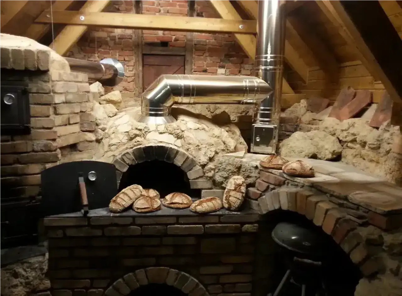Frisches Brot wird im Pizzaofen gebacken. Mehrere Laibe liegen bereit, um im heißen Ofen zu garen.