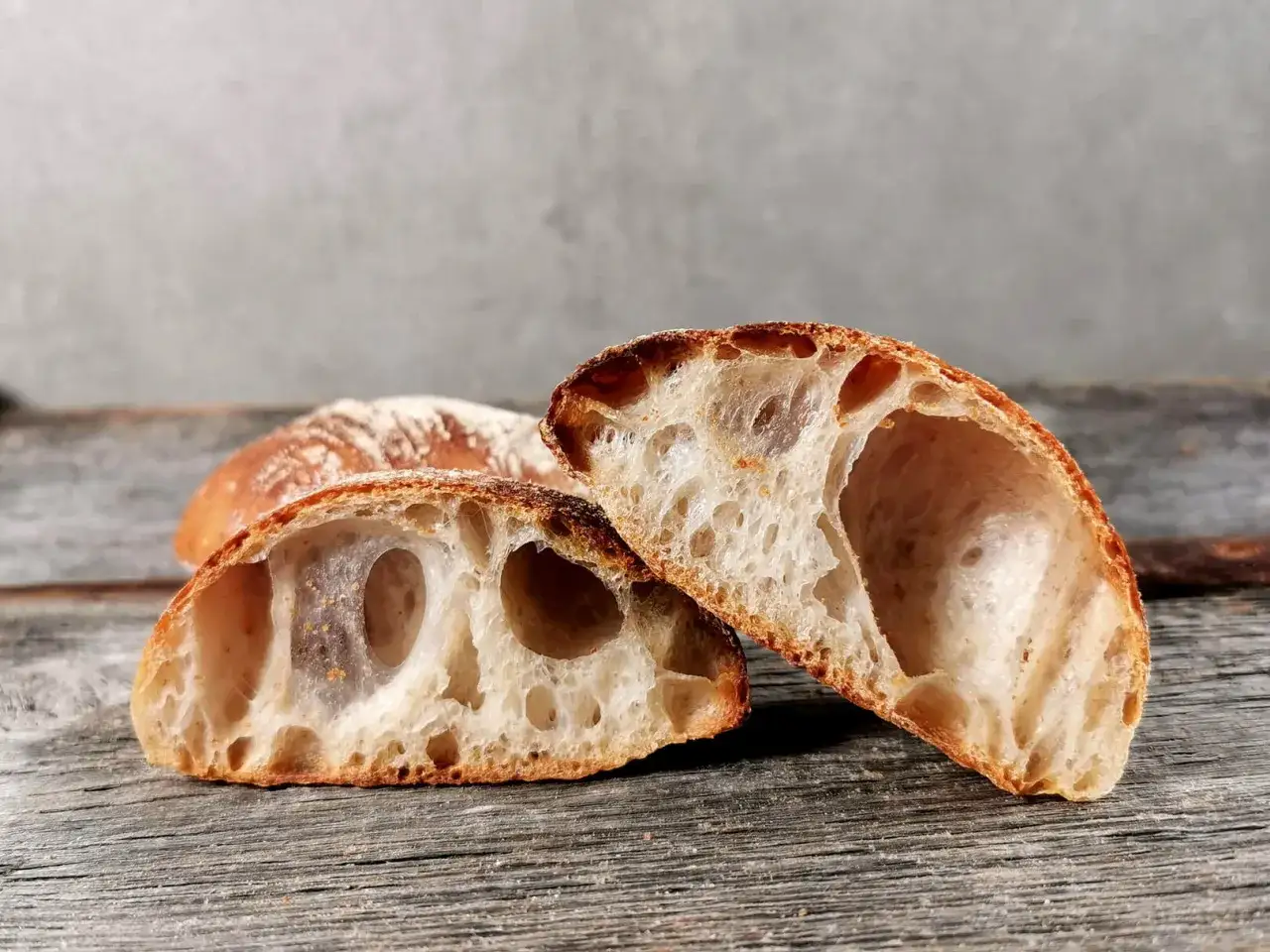 Zwei Hälften eines rustikalen ciabatta mit sauerteig Brotes liegen auf Holzbrettern. Die Krume ist luftig und voller großer Blasen.