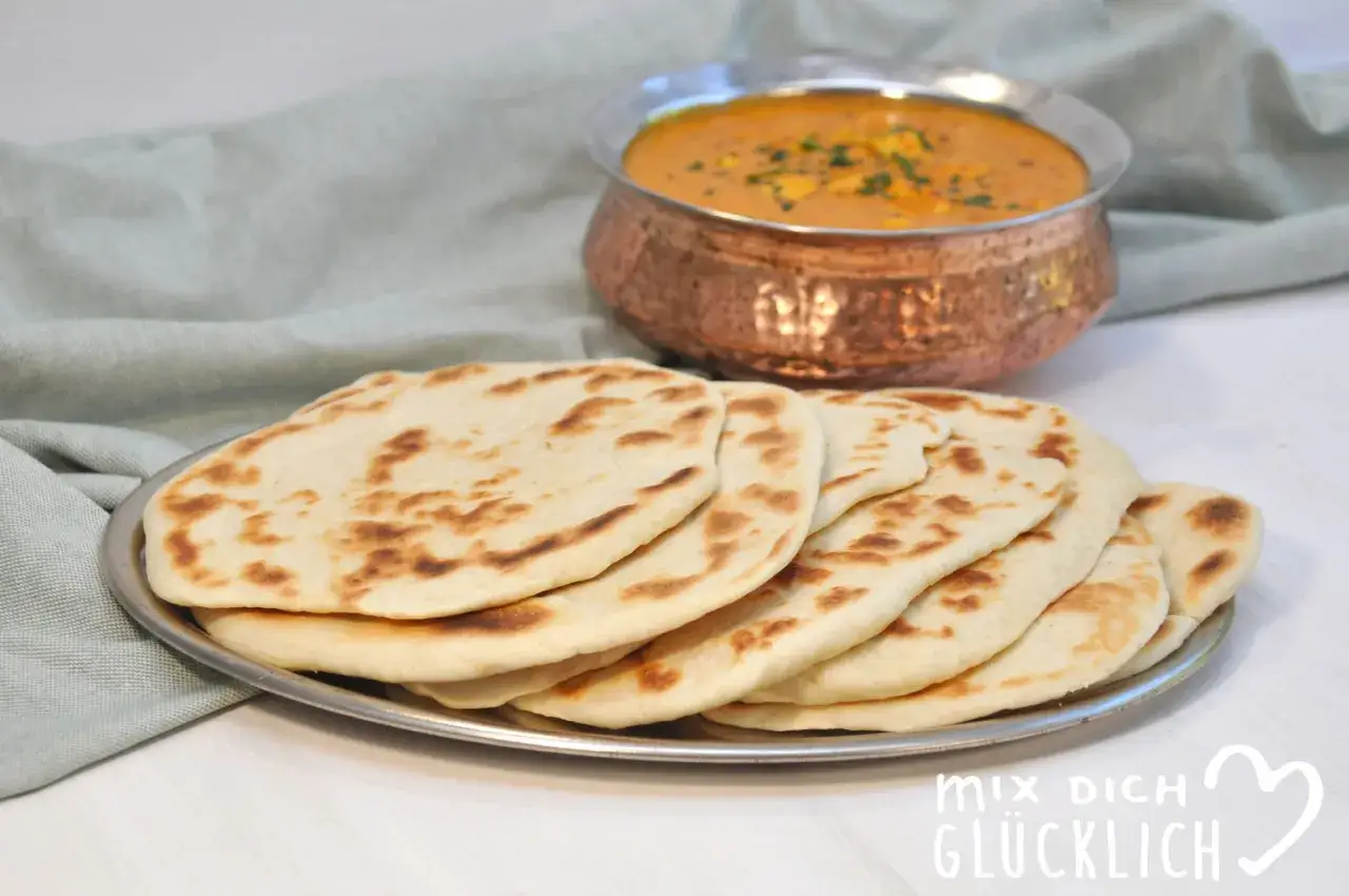 Frisch gebackenes Naan Brot liegt auf einem Teller, daneben eine Schüssel mit Curry. Perfekt für eine indische Mahlzeit!