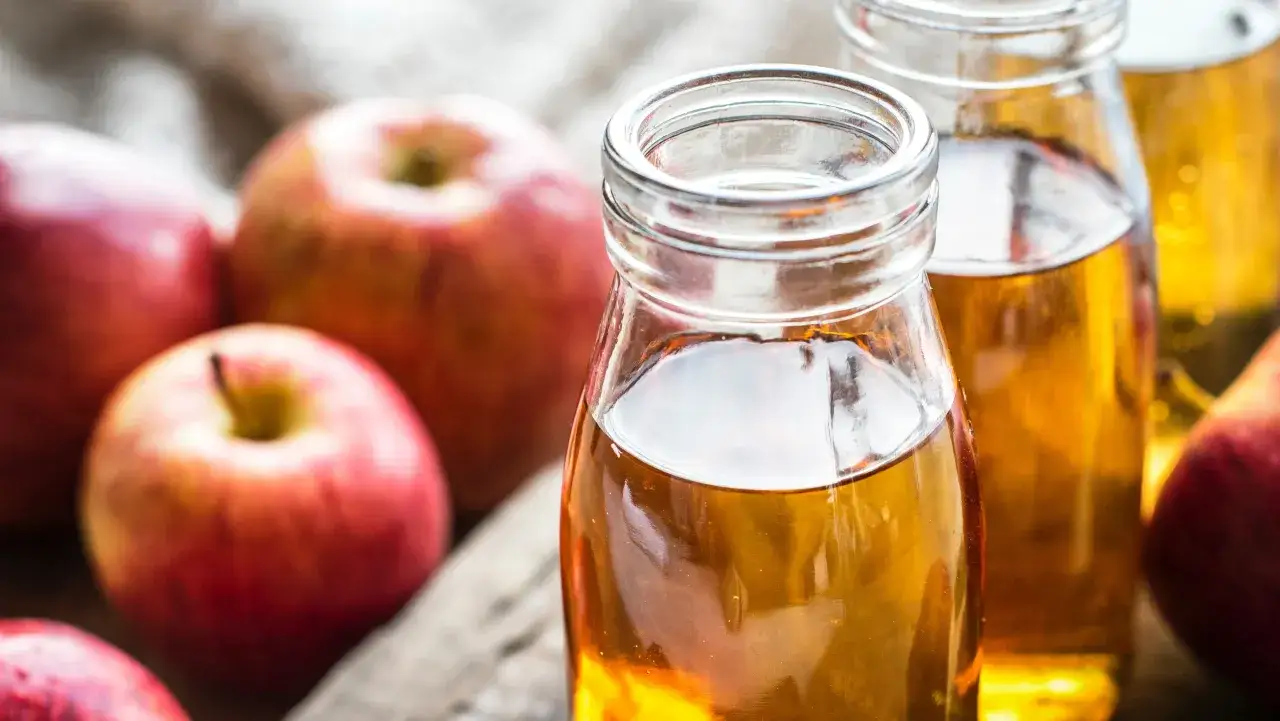 Frische Äpfel und Flaschen mit goldenem Apfelessig. Ein gesunder Trunk, der zum Apfelessig trinken einlädt.