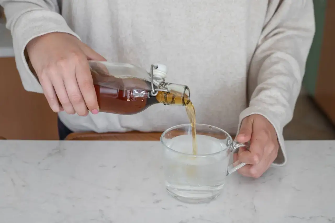 Eine Person gießt Apfelessig mit Wasser in ein Glas.