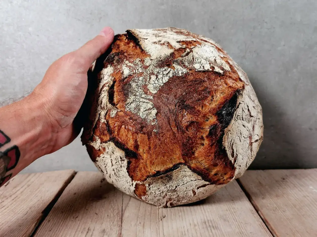 Hand hält ein rustikales bierbrot mit sauerteig, mit knuspriger Kruste und weichem Inneren, auf Holzbrettern.