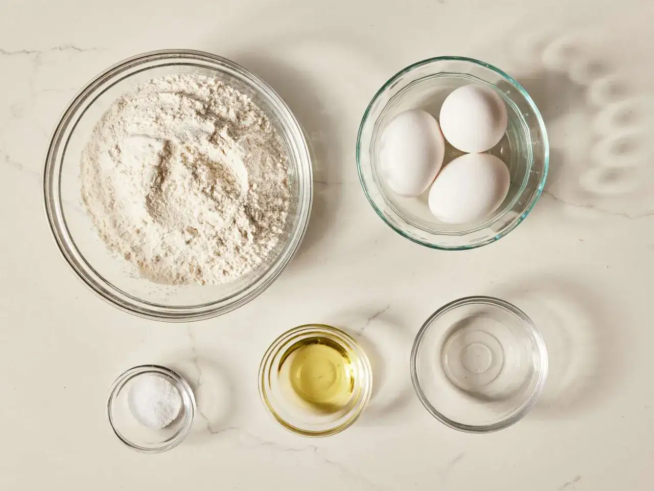 Zutaten für hausgemachte Nudeln: eine Schüssel mit Nudel Mehl, drei Eier, Salz, Öl und Wasser.