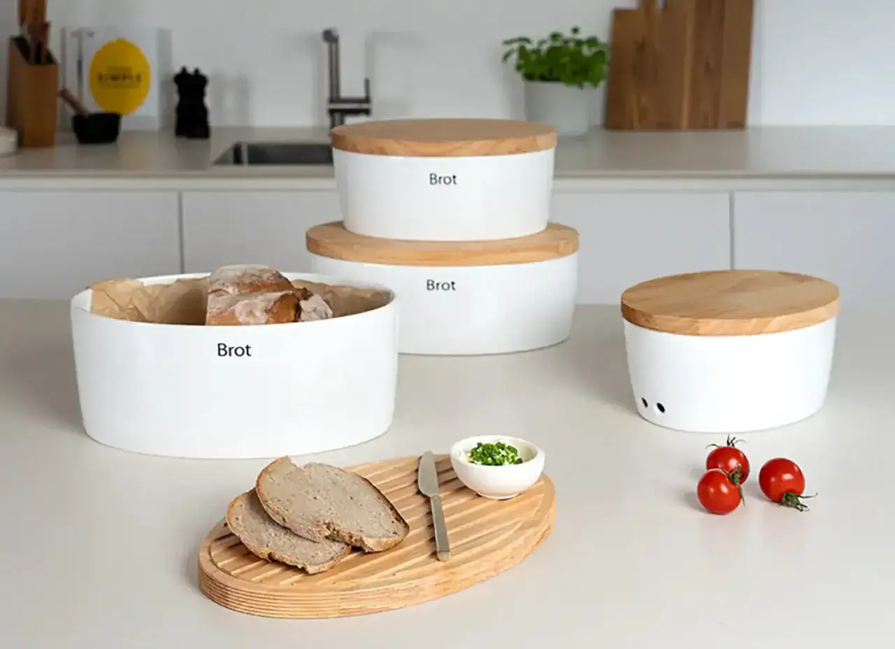 Mehrere weiße Brotdosen mit Holzdeckeln, ideal, um Brot frisch zu halten. Eine Dose ist mit Brot gefüllt, daneben liegen Brotscheiben.