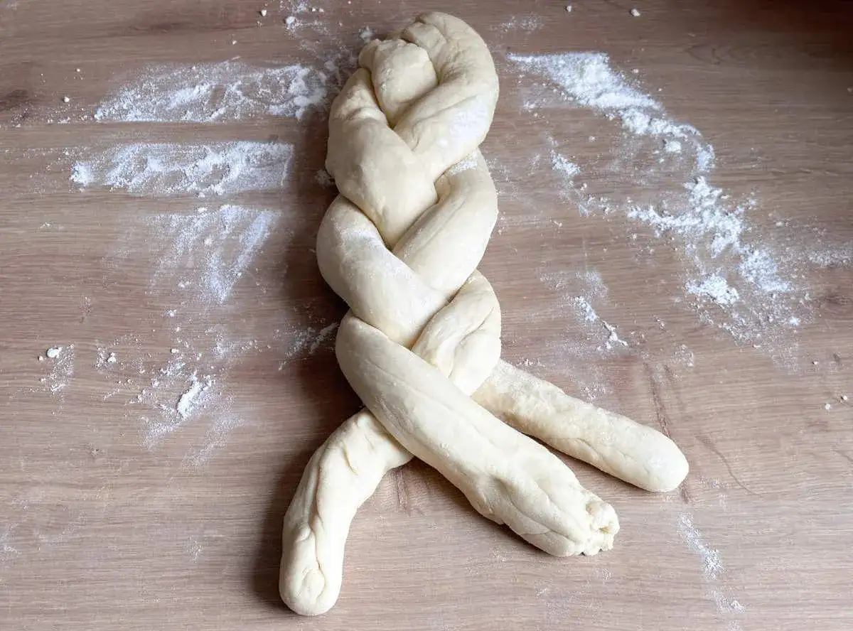 Ein frisch geflochtener Zopf Brot liegt auf einem Holztisch, bestäubt mit Mehl.