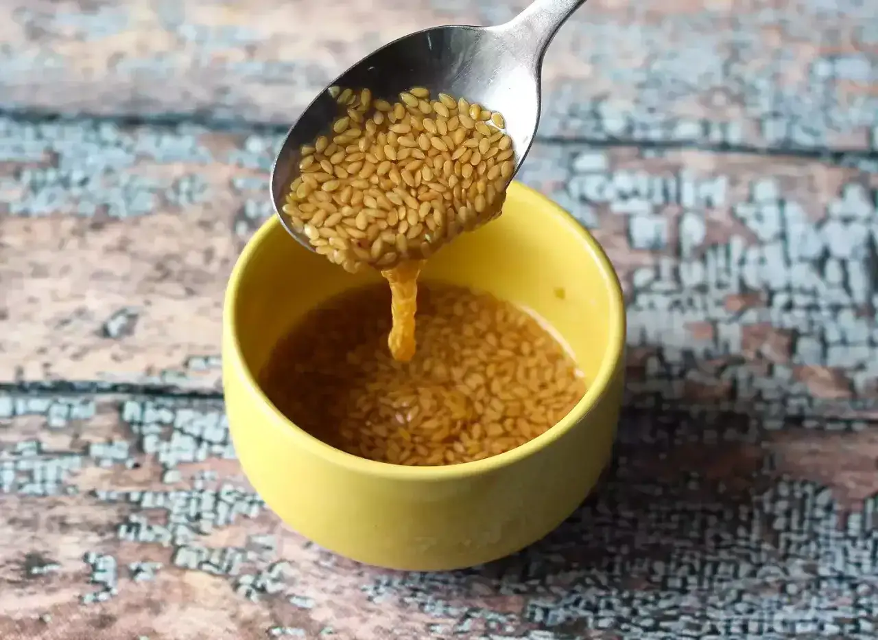 Ein Löffel voller Leinsamen wird in eine gelbe Schüssel mit Wasser gegossen. Die Leinsamen quellen auf und bilden eine gelartige Konsistenz, ähnlich einem Leinsamen-Ei.