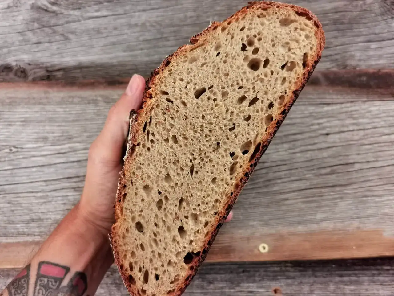 Eine Hand hält ein Stück Brot mit einer luftigen, hellbraunen brot krume und einer dunklen Kruste.