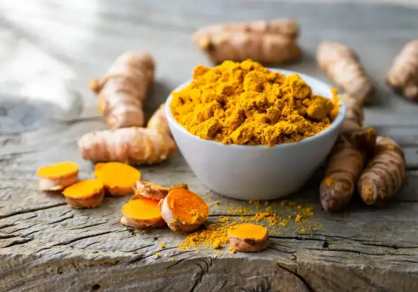 Kurkuma-Wurzeln und Pulver auf Holz. Informiert über die Frage: wieviel curcumin pro tag.