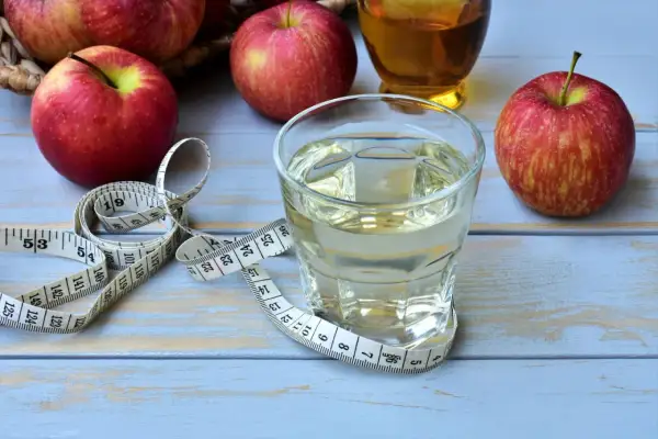 Ein Glas Apfelessig, Äpfel und ein Maßband. Ein täglicher Apfelessig-Schluck für die Gesundheit und eine schlanke Linie.