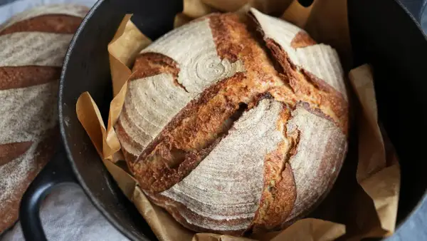 Ein frisch gebackenes Sauerteigbrot mit knuspriger Kruste liegt in einem Gusseisentopf. Perfekt für dein Sauerteigbrot Rezept!