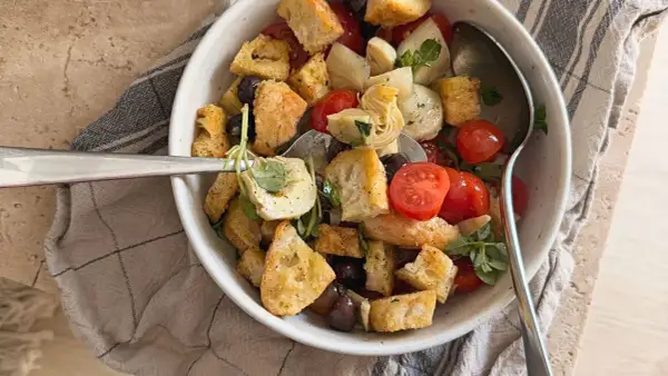 Herzhafter Brotsalat mit Roggenbrot, Kirschtomaten, Oliven und Artischockenherzen, garniert mit frischen Kräutern.