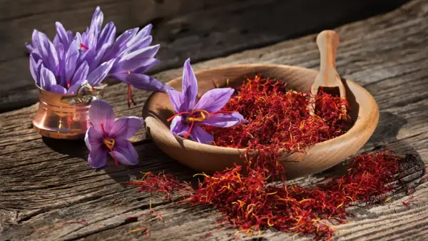 Safranfäden in einer Holzschale und lila Krokusblüten auf rustikalem Holz. Die **Safran Wirkung Gehirn** ist faszinierend, da das Gewürz für seine stimmungsaufhellenden Eigenschaften bekannt ist.