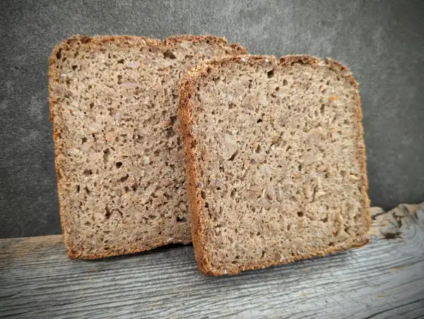 Zwei Scheiben rustikales **Kornbrot** liegen auf Holz. Das Brot ist dicht und voller Körner, mit einer dunklen Kruste.