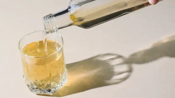Klarer Flüssigkeit wird aus einer Glasflasche in ein Glas gegossen. Ein gesunder Schluck Essigwasser für den Tag.